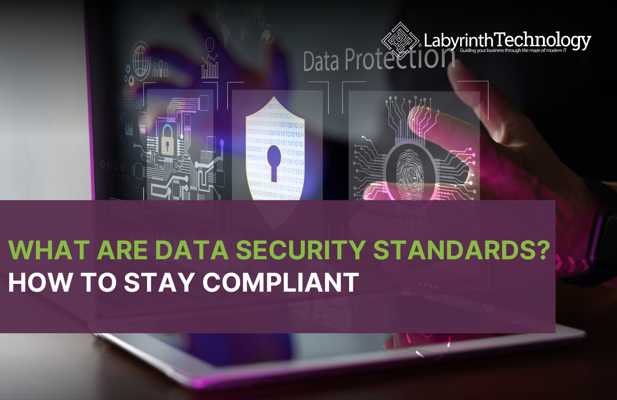 A man with his laptop and tablet, there are holographic cards with various cyber security related icons. the text says "what are data security standards? how to stay compliant." The labyrinth techology logo is in the top right